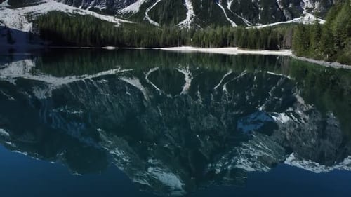 Snow-covered mountain peaks towering over a serene alpine lake surrounded by dense forest