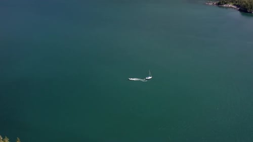 Inflatable Motor Boat Leaving Yacht Floating On Calm Waters In Alaska. - aerial static