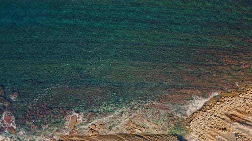 Agua de mar cristalina que lava piedra rugosa, vista desde arriba, olas y salpicaduras