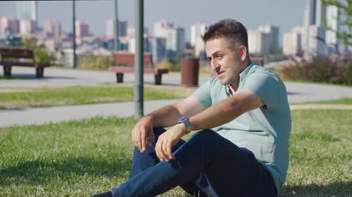 Man Sitting on Grass in City Park Thinking