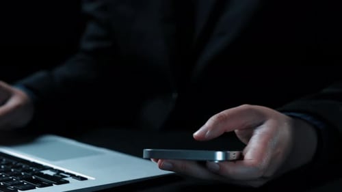 Man Types on Laptop, Education Icons on Phone