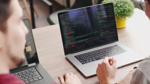 Two Hipster Coworkers Sharing Ideas About Project Sitting with Laptops in Spacious Open Space Office
