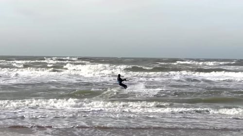 Surfer with kite jumping over large waves during cloudy day in Netherlands - Wide shot