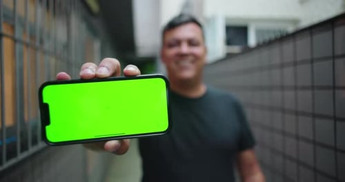 Homem sorridente assistindo conteúdo no smartphone e, em seguida, estendendo o telefone em direção à câmera com personalizável