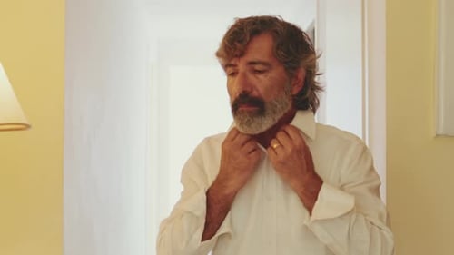 Man Buttons a White Shirt Indoors