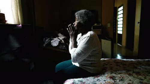 Senior Woman Sitting on Bed with Hands Clasped