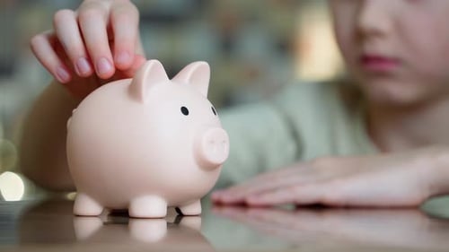 Close-up of a boy putting coins into a piggy bank.