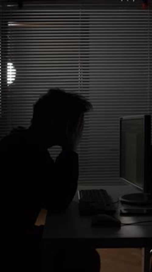 Vertical Video Man Silhouette Working Late at Computer Desk in a Dark Office Blinds on Window