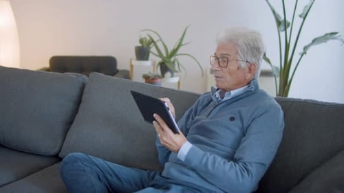 Senior Man Relaxing on Couch Using Tablet
