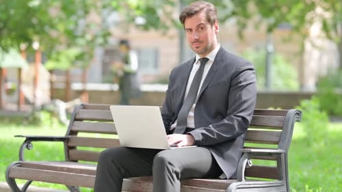 Thumbs Down by Middle Aged Businessman Using Laptop Outdoor on Bench