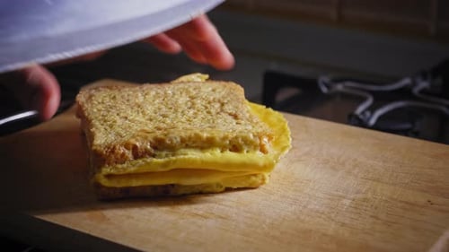 A close up shot of the hands of a chef positioning a sandwich before slicing through the middle with
