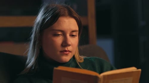 Concentrated Woman Reading Book in Dimly Lit Room