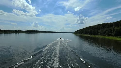 Wakesurfer training wake boarding skills behind the boat down the river waves, aerial view.