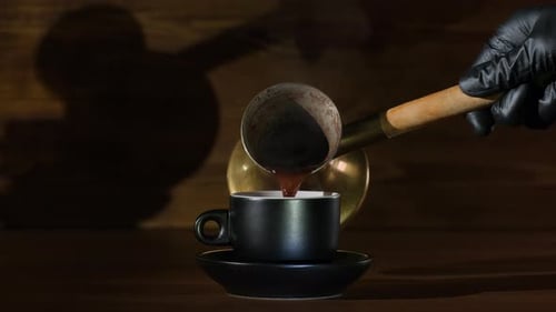 Pouring coffee from a golden copper cezve into a black cup