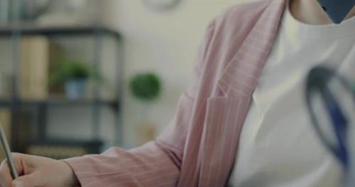 Tiltup Portrait of Young Employee Writing in Notebook and Speaking on Mobile Phone in Office