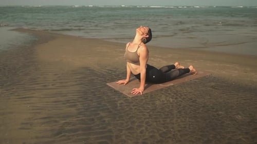 Profesor de yoga inclinando la espalda hacia arriba mirando al perro mientras imparte una clase junto a la playa.