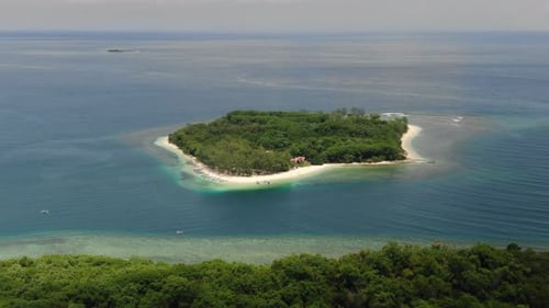 Aerial wide shot as approaching a tropical island in the ocean, flying over a forest at a white sand