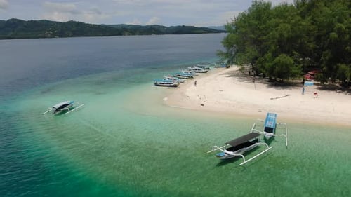 Aerial orbital shot around a tropical island, as boats waiting on the white sand beach in the middle
