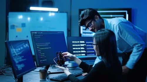 Tech engineers collaborate on a modern robotics project in a high-tech lab at night, analyzing code