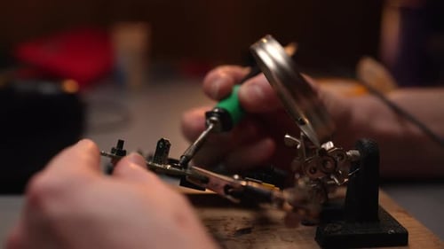 Nahaufnahme der Hände eines nicht wiederzuerkennenden Technikers, der mit Hilfe von Lötkolben eine Leiterplatte repariert