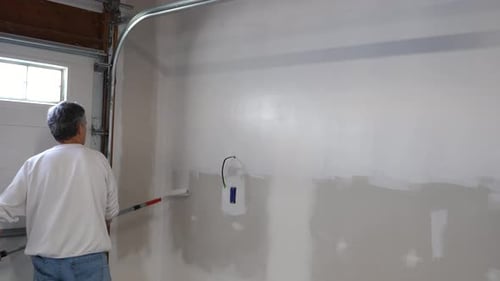 Adult Man Using Paint Roller in Garage - White Primer on Walls - Home Renovation