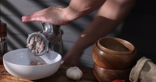 Man making minced meat with grinder at wooden table, closeup