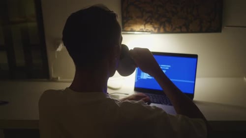 Young Man Works On Laptop At Desk at Night