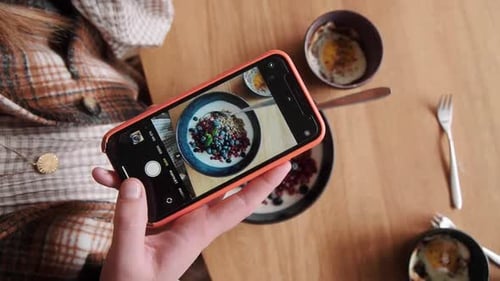 Top Shot of female influencer taking a picture of her breakfast granola bowl with her phone at home.