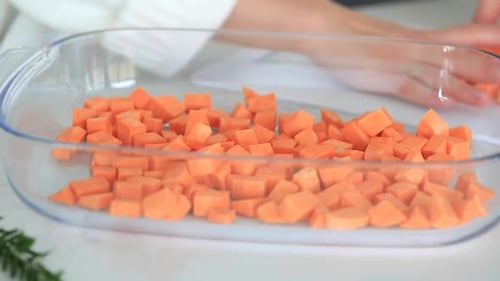 Uma mulher coloca pedaços de batata-doce em uma assadeira de vidro no forno