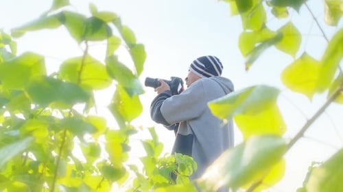 Photographer holding camera points and shoots in nature park scene, bright sky, dreamy effect