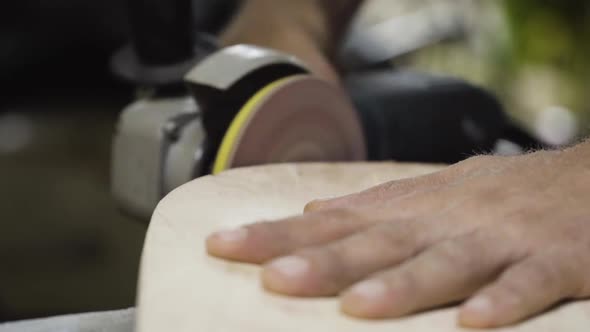 Closeup, man using orbital disc sander to smooth side of DIY skateboard ...
