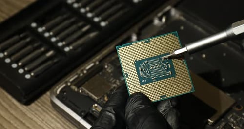 Man repairing central processing unit of laptop with screwdriver at wooden table, closeup