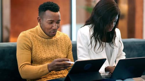 Black man and woman working using tablet and laptop in an office, discussing business affairs while