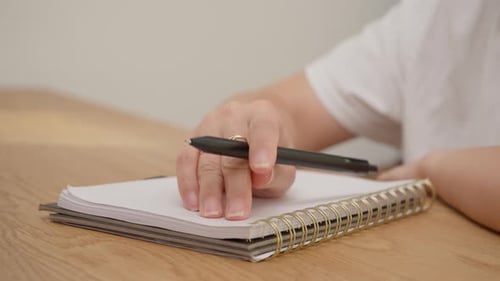 Female hand rhythmically tapping black pen on spiral notebook page with audio