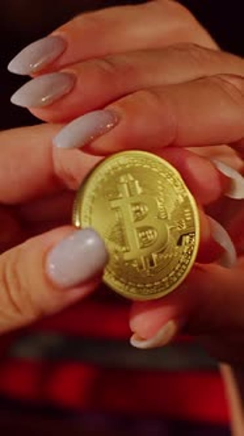 Vertical video. Close Up Shot Of Female Hand With Manicure Holding Golden Bitcoin Coin In Soft Warm