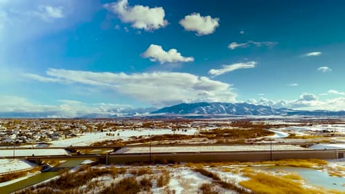 A highway through a urban area and snowy landscape with mountains n the distance - aerial hyperlapse