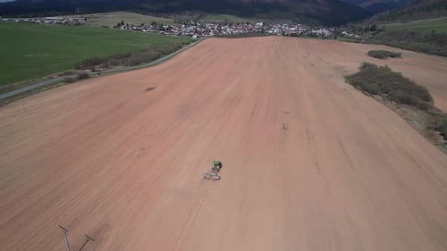 Vue aérienne par drone d'un tracteur avec rouleaux et charrue sur des terres agricoles poussiéreuses