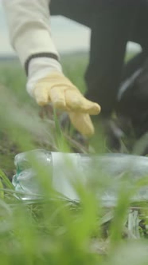 Man Collecting Plastic Bottles Outdoors Volunteer Removing Plastic Debris From Wet Grassy Area for