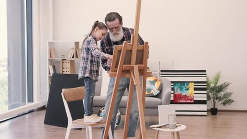 Older Grandpa Teaching Painting to Small Girl Indoors