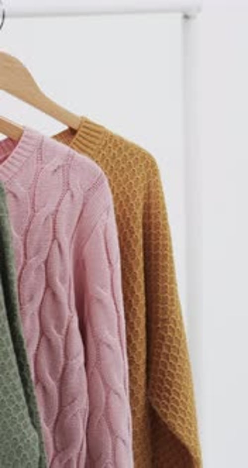 Vertical video of three multi coloured sweaters on hangers and copy space on white background