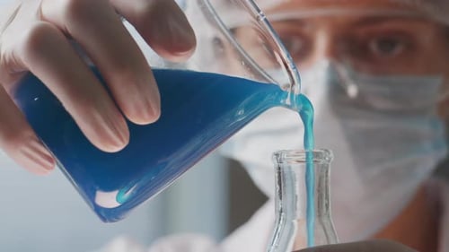 Científico vierte líquido azul de un vaso de precipitados en un matraz durante un trabajo de laboratorio