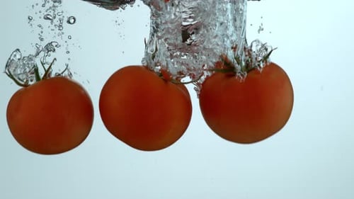 Three Orange Tomatoes Splashing Into Water on White