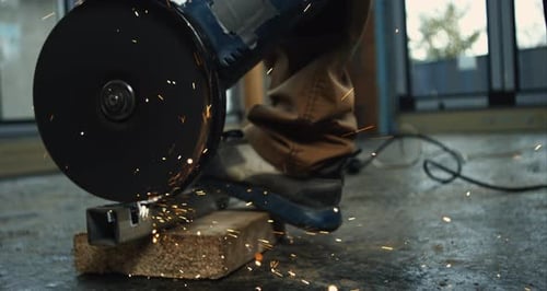 Grinding metal bar on brick block, worker’s hands steadying grinder, shower of sparks, intense