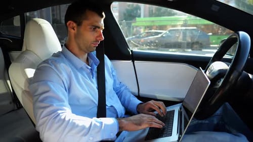 Handsome Entrepreneur Working on Notebook While Riding an Autonomous Self Driving Electric Car at