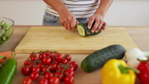 Close Up Woman Hands Slicing Fresh Cucumber on Wooden Cutting Board in Kitchen