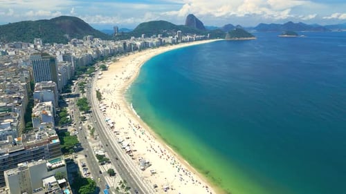 Aerial View of a Bustling Beach Adjacent to a Vibrant City Coastline with Lush Green Mountains in