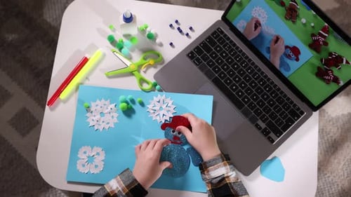 Artesanía infantil hecha a mano. Niño haciendo postales de Navidad mediante un tutorial en vídeo en la mesa. Cámara en movimiento