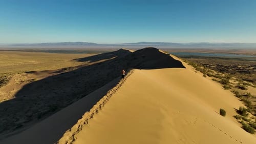 Lone figure on a desert dune overlooking a lake and mountains