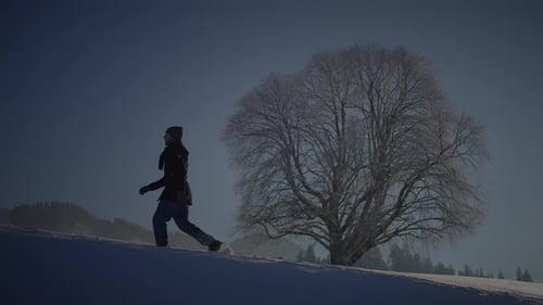 Man Walks up Snowy Hill Past Tree