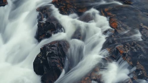 Vidéo à exposition longue qui montre un puissant flux d'eau vive au-dessus des roches foncées et écaillées.